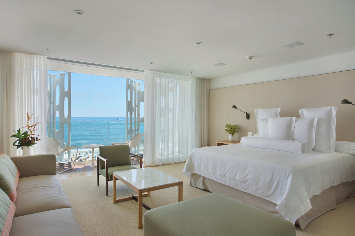 A hotel room with a large bed, a sofa, a table, and a view of the ocean.