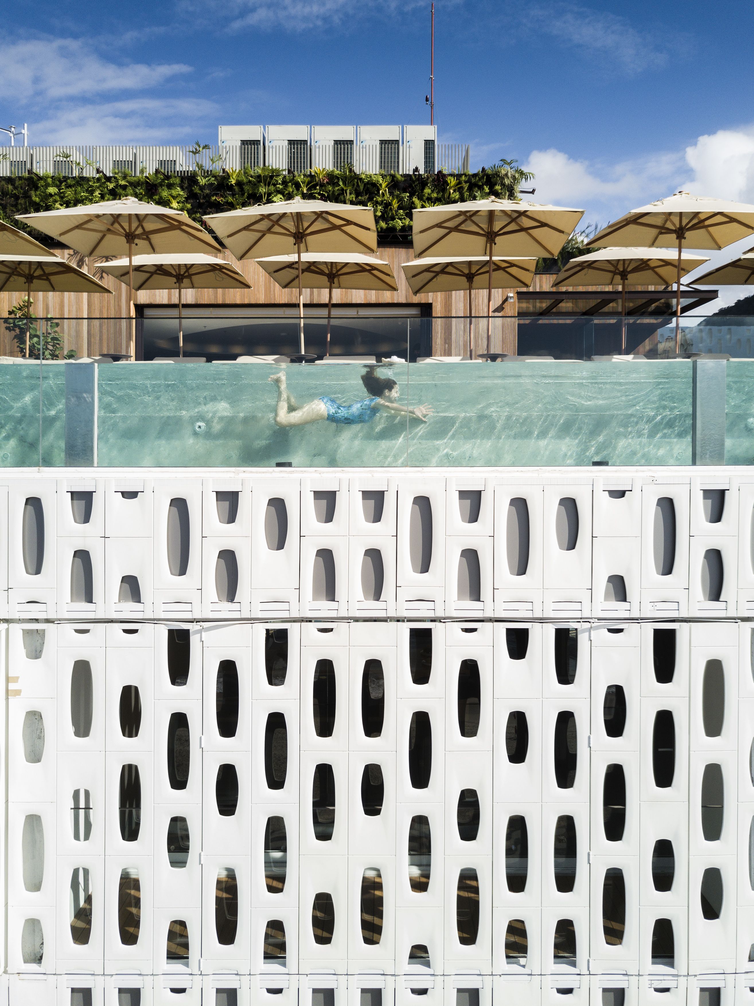 A swimming pool with a person swimming, surrounded by umbrellas and a building with a modern design.