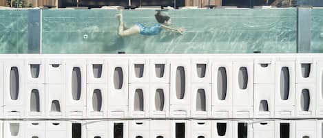 A swimming pool with a person swimming, surrounded by umbrellas and a building with a modern design.