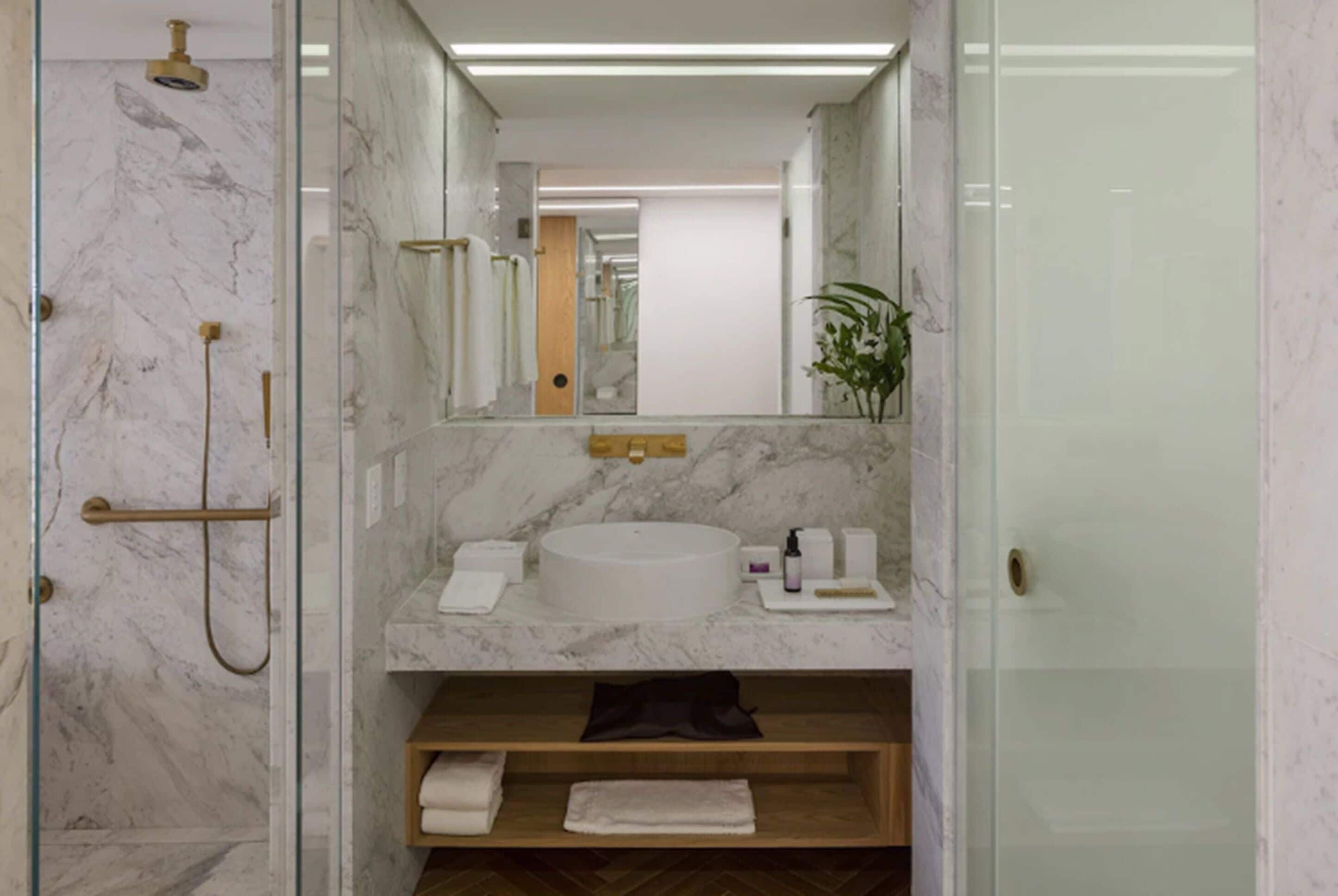 A modern bathroom with a marble shower, a round sink, and a wooden shelf with towels.