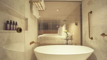 A modern bathroom with a freestanding bathtub, marble walls, and a visible shower area.