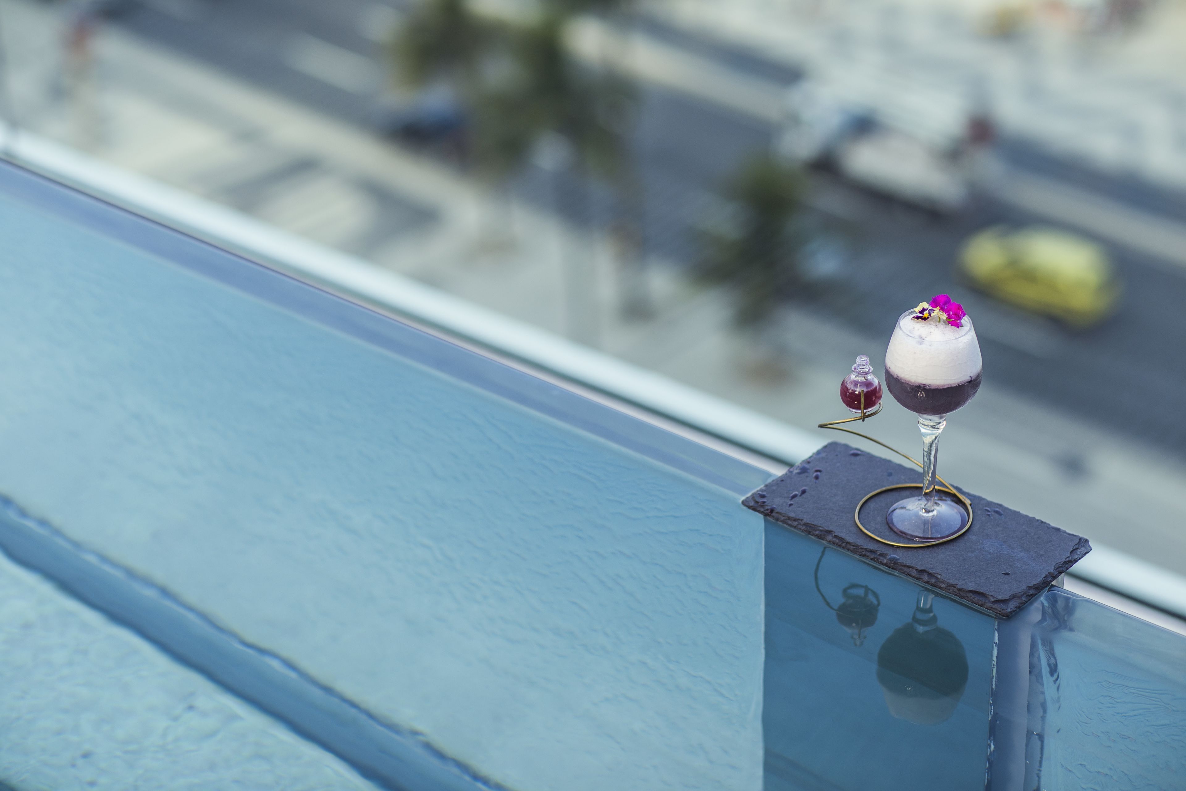 Un vaso de bebida sobre una barandilla de balcón con vistas a la ciudad.