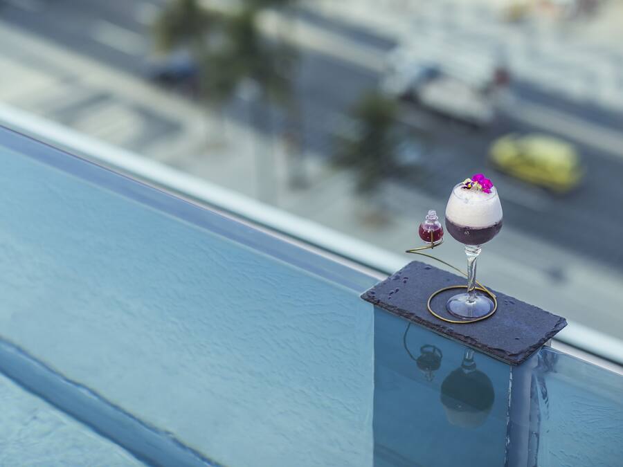 Un vaso de bebida sobre una barandilla de balcón con vistas a la ciudad.