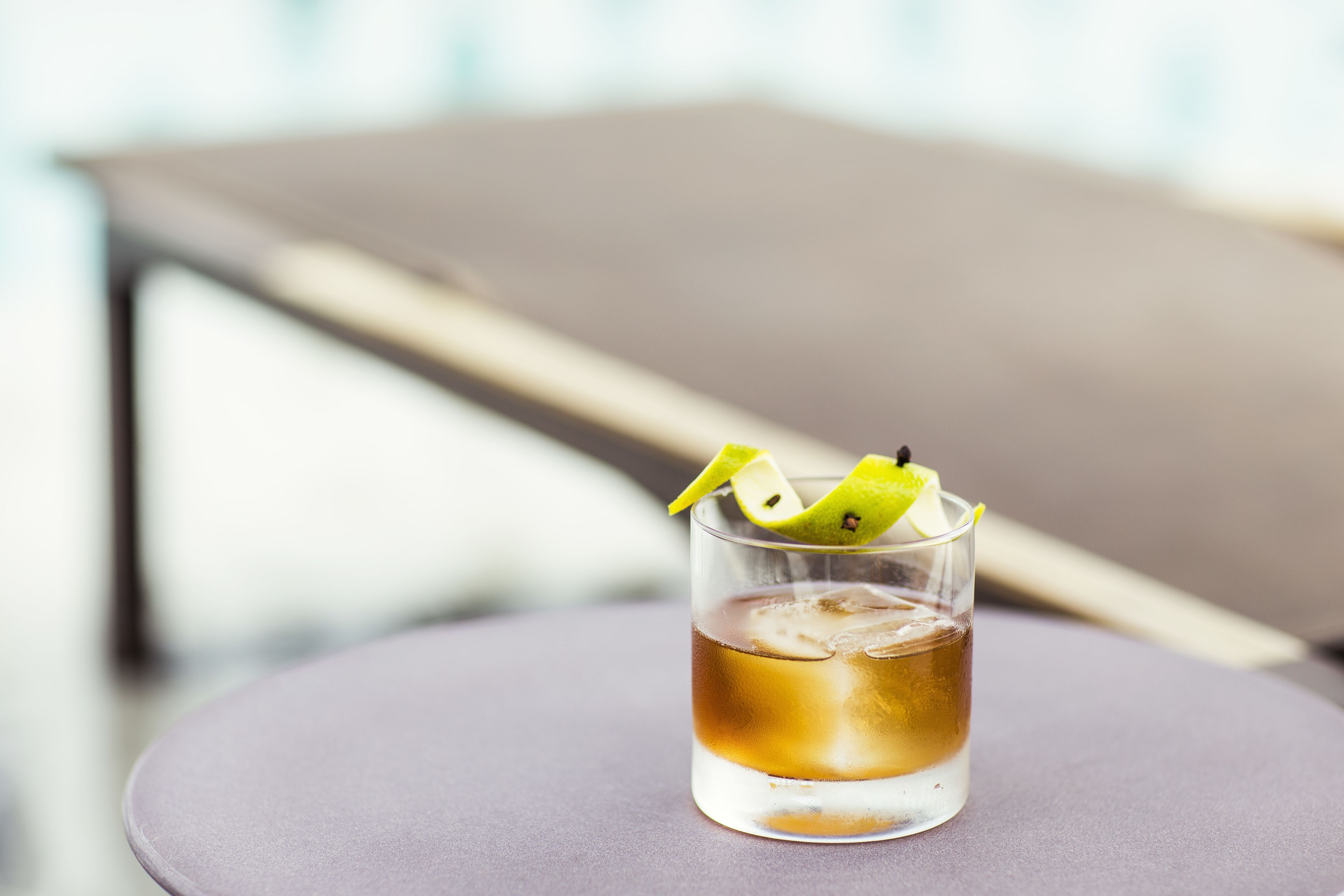 A glass of amber-colored beverage with ice cubes and lime slices on a round table.