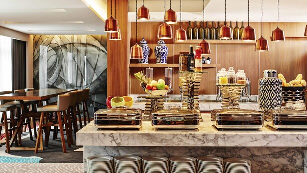 A modern hotel dining area with a marble counter, hanging copper pendant lights, and a variety of food and drink items. - Mercure Kuala Lumpur Shaw Parade (Kuala Lumpur)