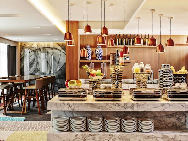 A modern hotel dining area with a marble counter, hanging copper pendant lights, and a variety of food and drink items. - Mercure Kuala Lumpur Shaw Parade (Kuala Lumpur)