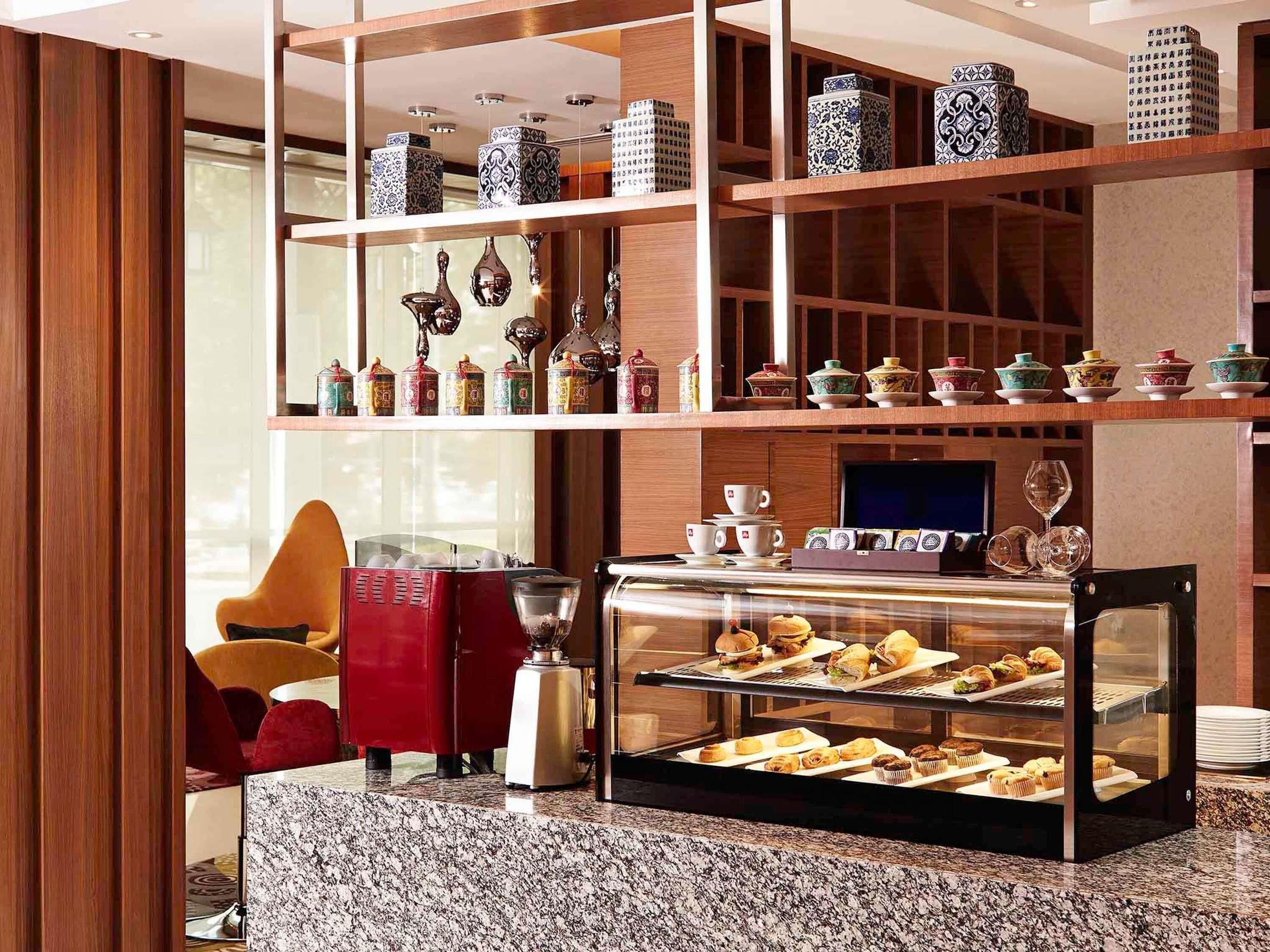A hotel lobby with a coffee station, a TV, and shelves with decorative items.