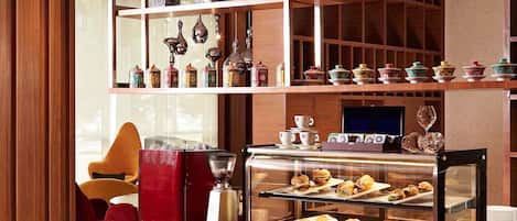 Un vestíbulo de hotel con una estación de café, un televisor y estanterías decorativas.