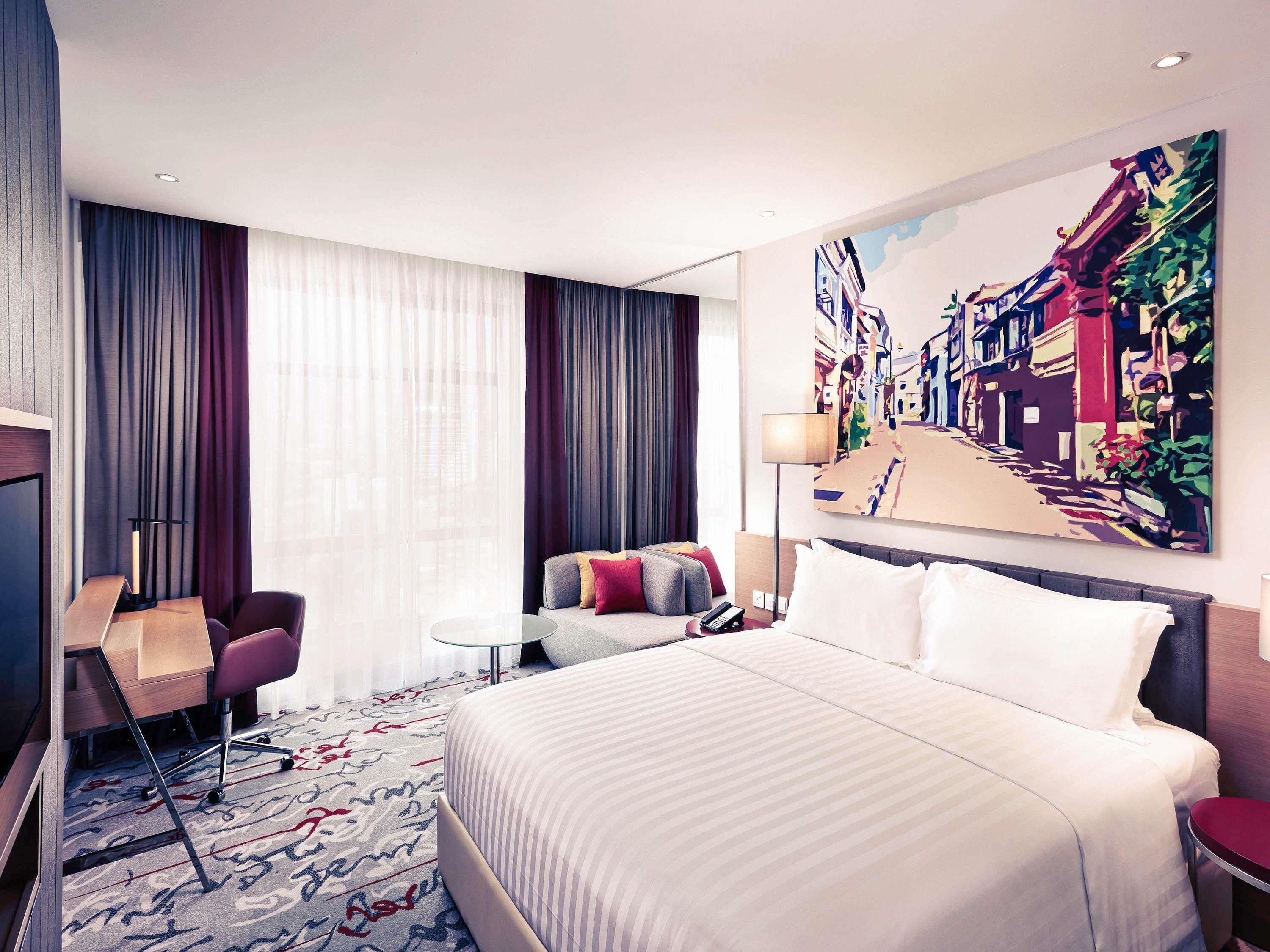 Une chambre d’hôtel avec un grand lit, un bureau, une chaise, une petite table et un tableau au mur.