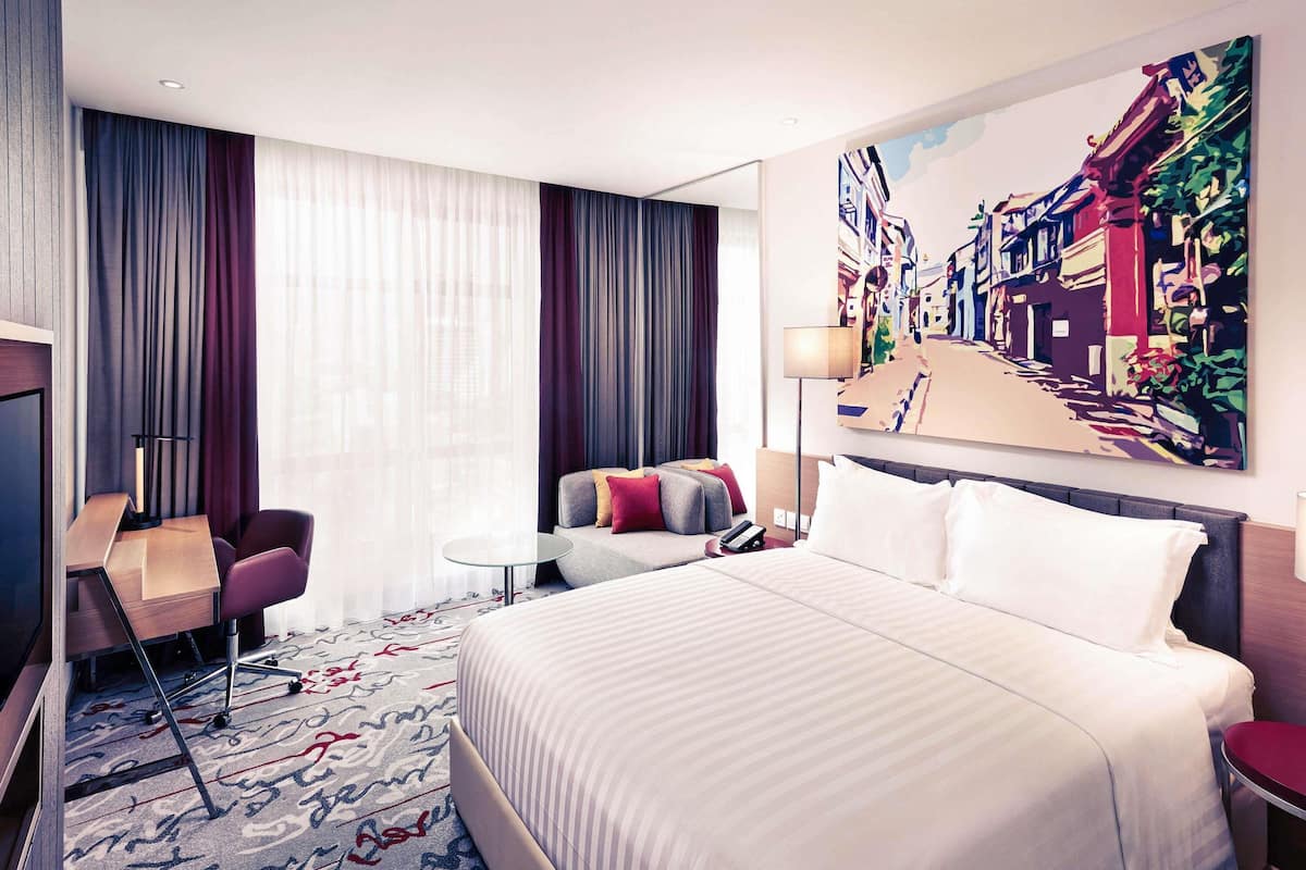 Une chambre d’hôtel avec un grand lit, un bureau, une chaise, une petite table et un tableau au mur.