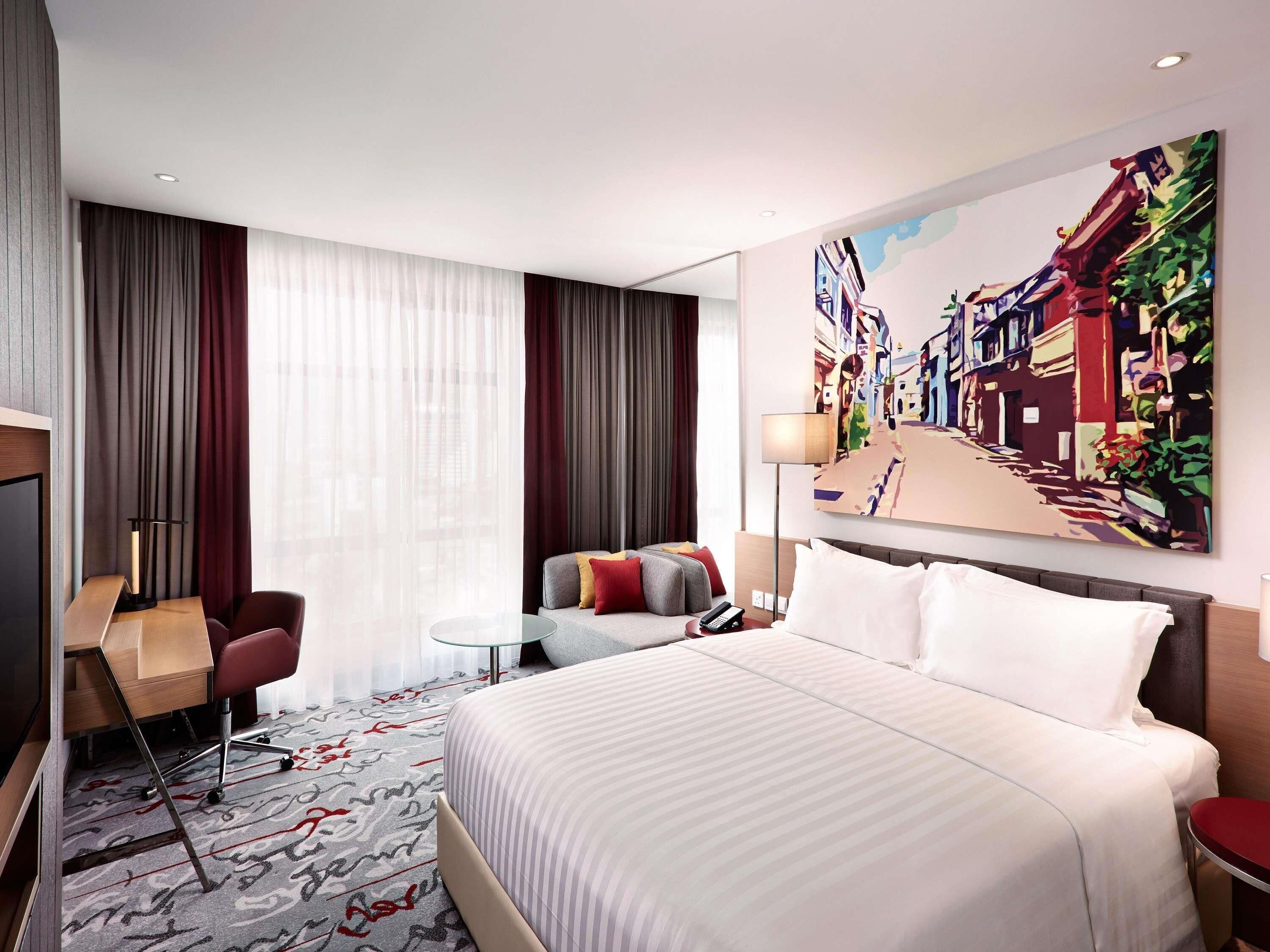 Une chambre d’hôtel avec un grand lit, un bureau avec une chaise, une petite table et un tableau au mur.