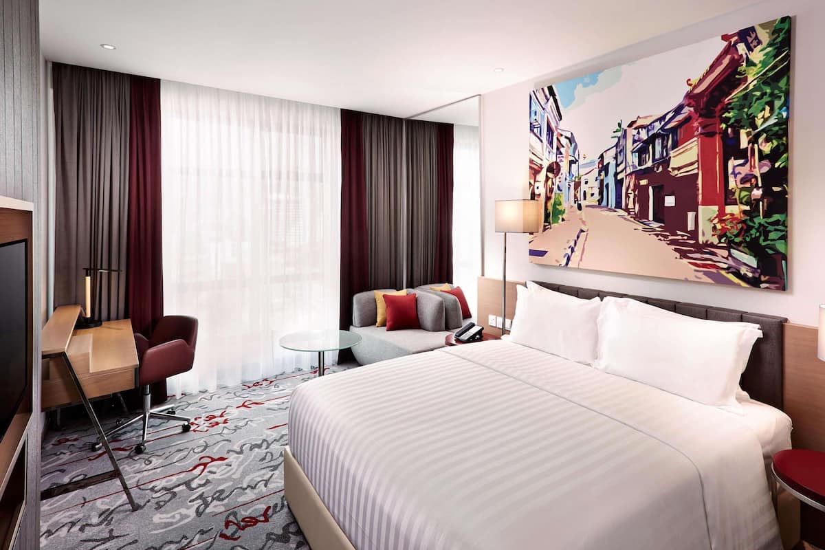 Une chambre d’hôtel avec un grand lit, un bureau avec une chaise, une petite table et un tableau au mur.