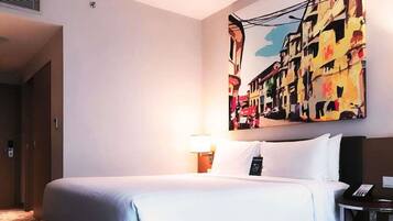 A hotel room with a bed, a bedside table with a lamp, a phone, and a large abstract painting on the wall.