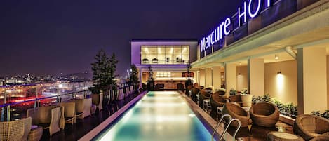 Un hôtel doté d'une piscine, de meubles en osier et offrant une vue sur la ville la nuit.