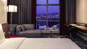 A hotel room with a bed, a sofa, a desk, and a view of a cityscape through a large window. - Mercure Kuala Lumpur Shaw Parade (Kuala Lumpur)