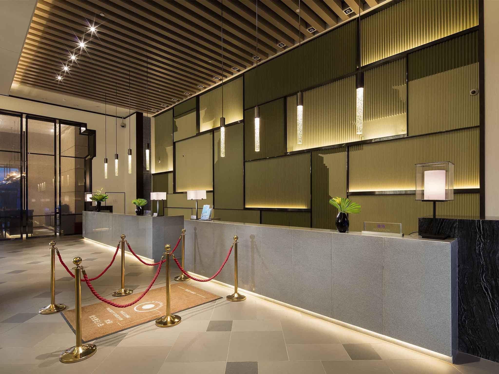 Zona de recepción de hotel con diseño moderno, que incluye un mostrador de recepción, una barrera de cuerda roja y un suelo estampado.