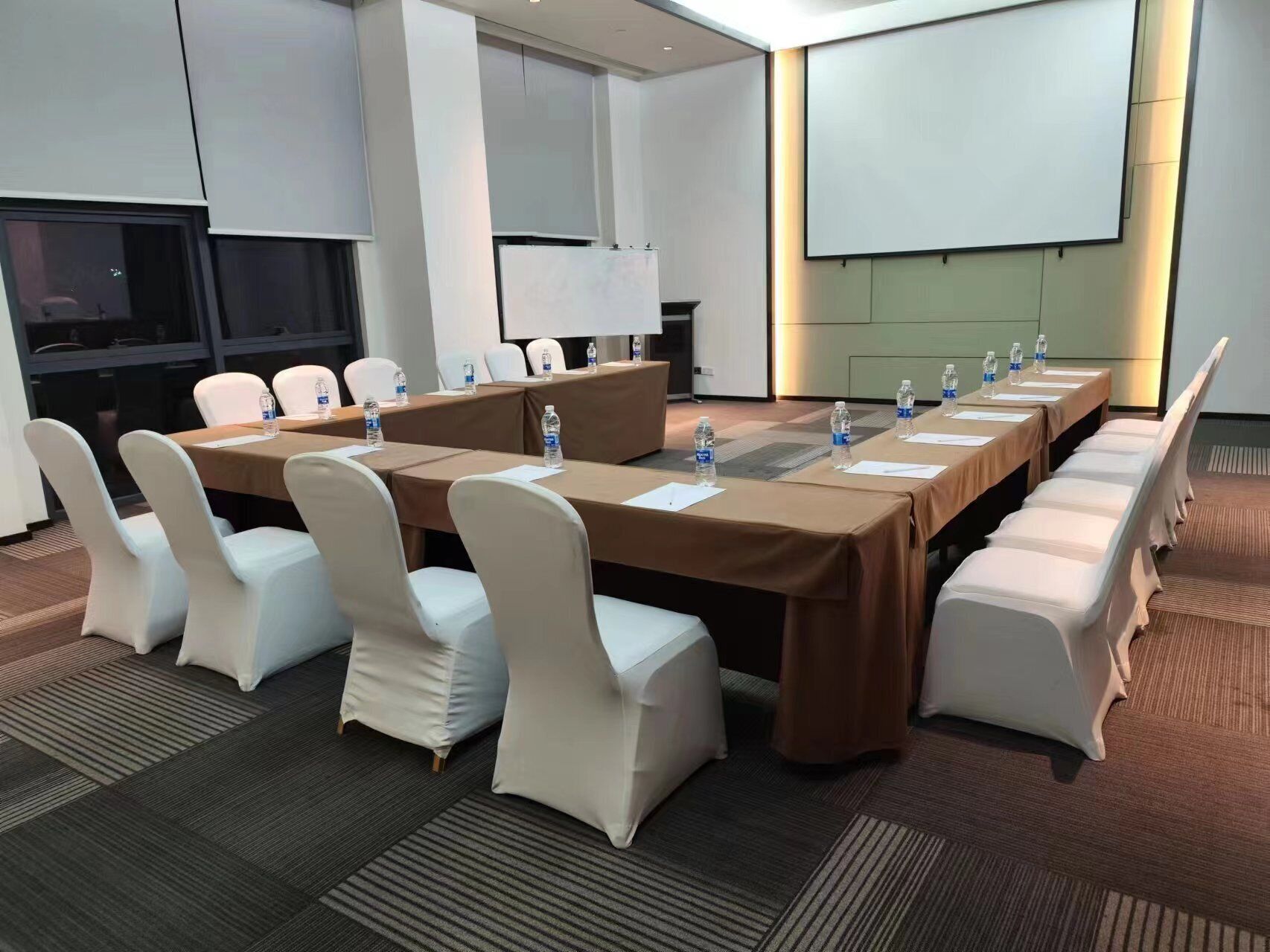 A conference room with a long table, white chairs, water bottles, and a projector screen.