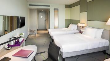 A hotel room with two beds, a desk with a laptop, a chair, a TV, and a bathroom door.
