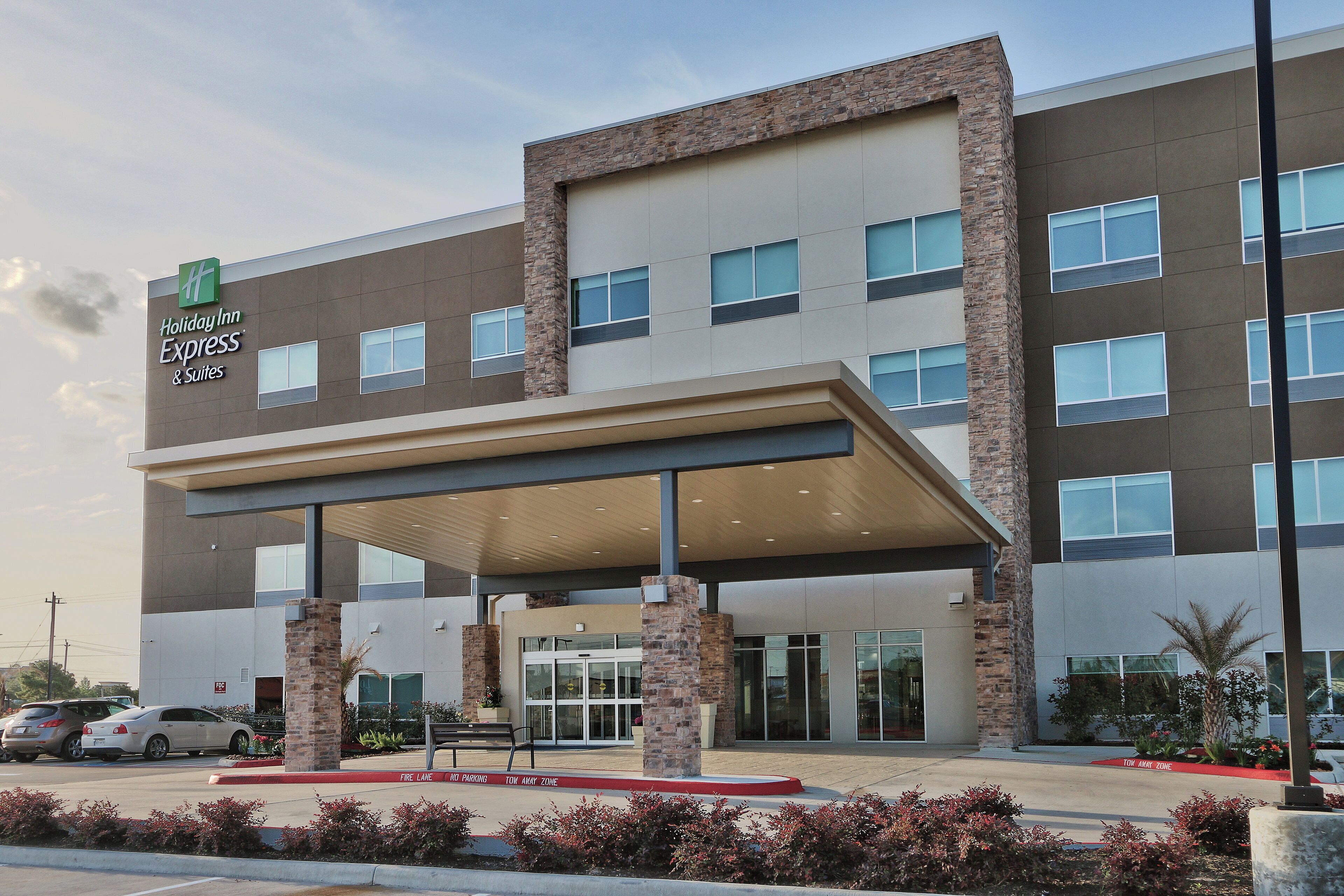 A Holiday Inn Express & Suites building with a covered entrance, multiple windows, and a fire lane.