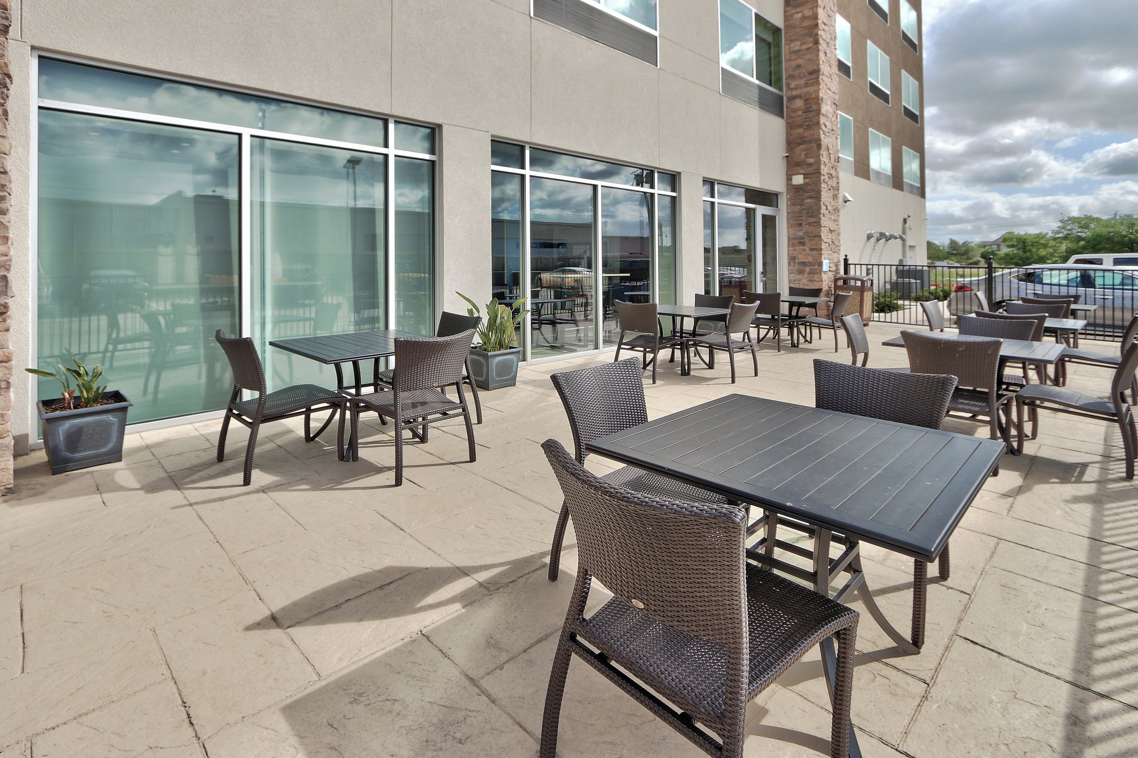 An outdoor patio area with tables and chairs, large windows, and a brick building facade.