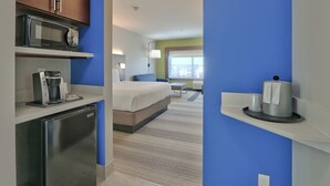 A hotel room with a kitchenette, a bed, a desk, and a view of the city. - Holiday Inn Express & Suites Houston East - Beltway 8 by IHG (Houston)