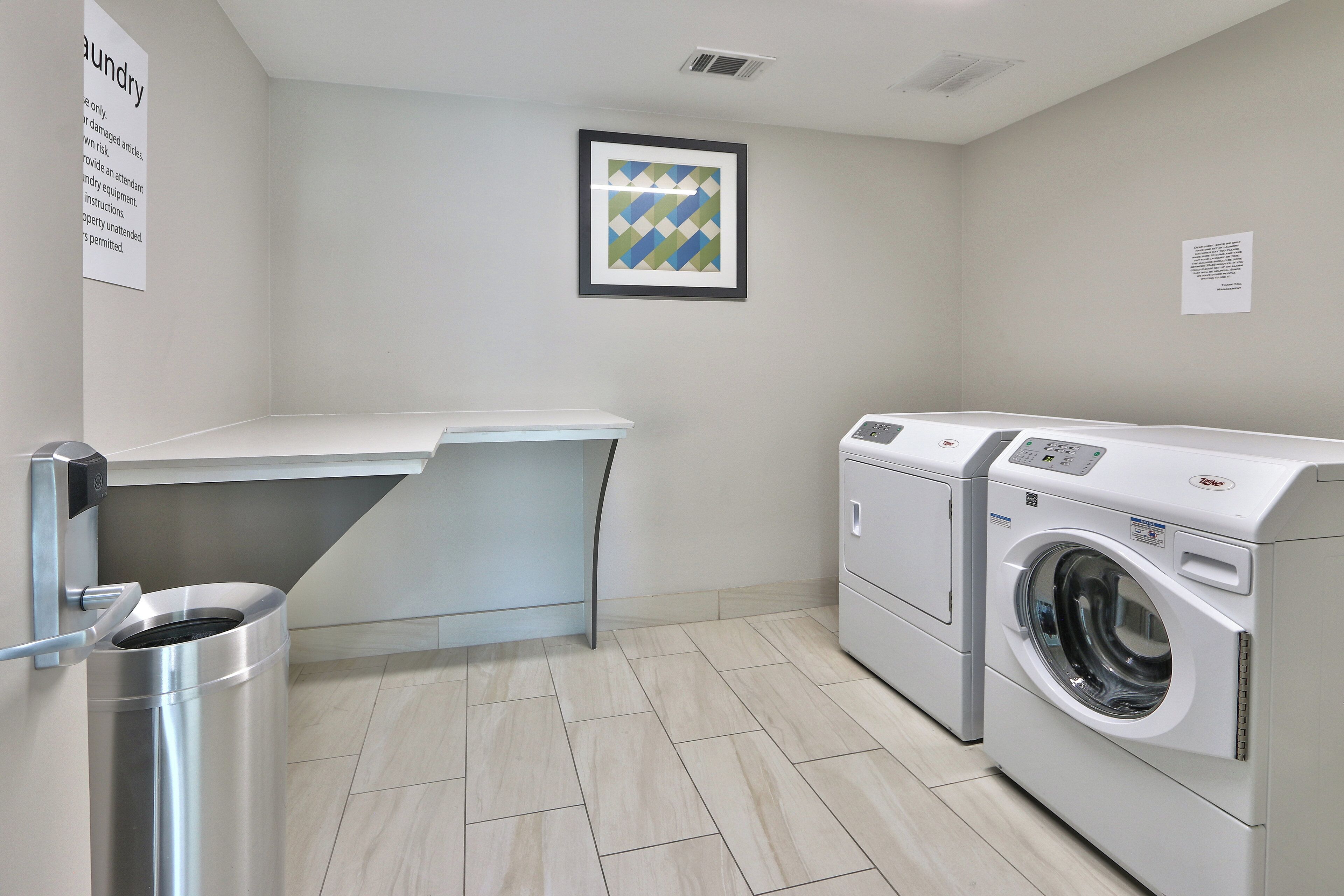 A laundry room with a washing machine, a drying rack, and a trash bin.
