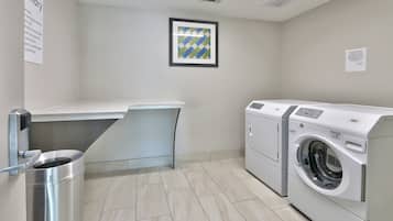 A laundry room with a washing machine, a drying rack, and a trash bin.