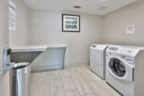 A laundry room with a washing machine, a drying rack, and a trash bin. - Holiday Inn Express & Suites Houston East - Beltway 8 by IHG (Houston)