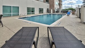 A swimming pool with lounge chairs, a brick building, and a gated entrance. - Holiday Inn Express & Suites Houston East - Beltway 8 by IHG (Houston)