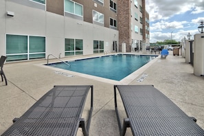 A swimming pool with lounge chairs, a brick building, and a gated entrance. - Holiday Inn Express & Suites Houston East - Beltway 8 by IHG (Houston)
