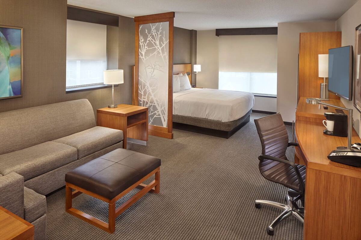 A hotel room with a bed, a sofa, a desk with a chair, a TV, and a window.