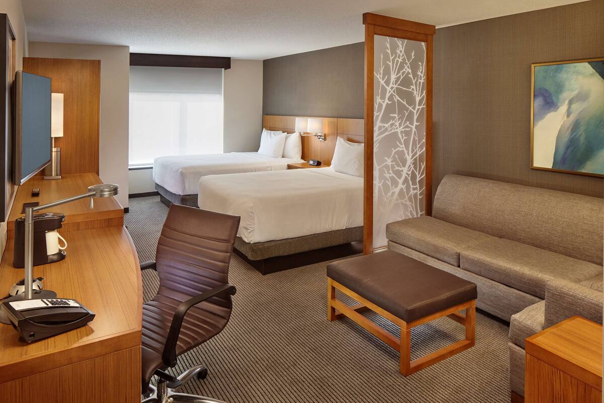 A hotel room with two beds, a sofa, a desk with a computer, and a TV.