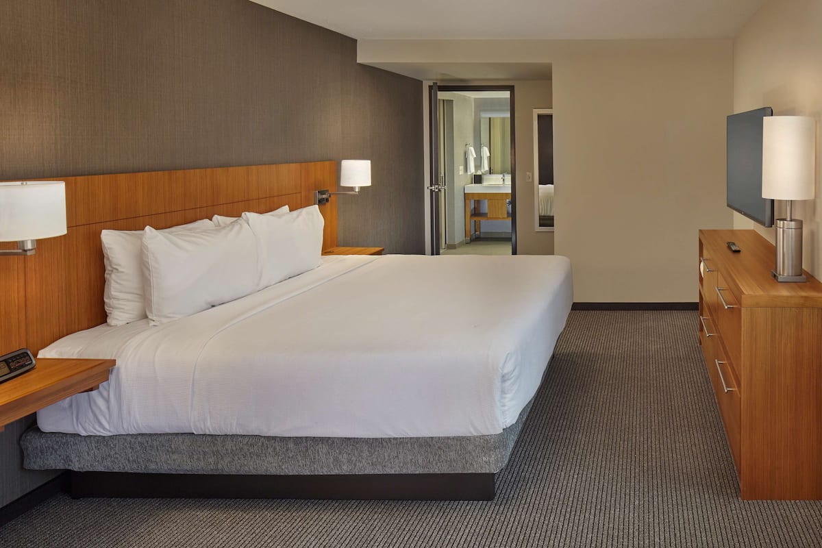 A hotel room with a large bed, wooden headboard, bedside tables with lamps, a wooden dresser, and a television.