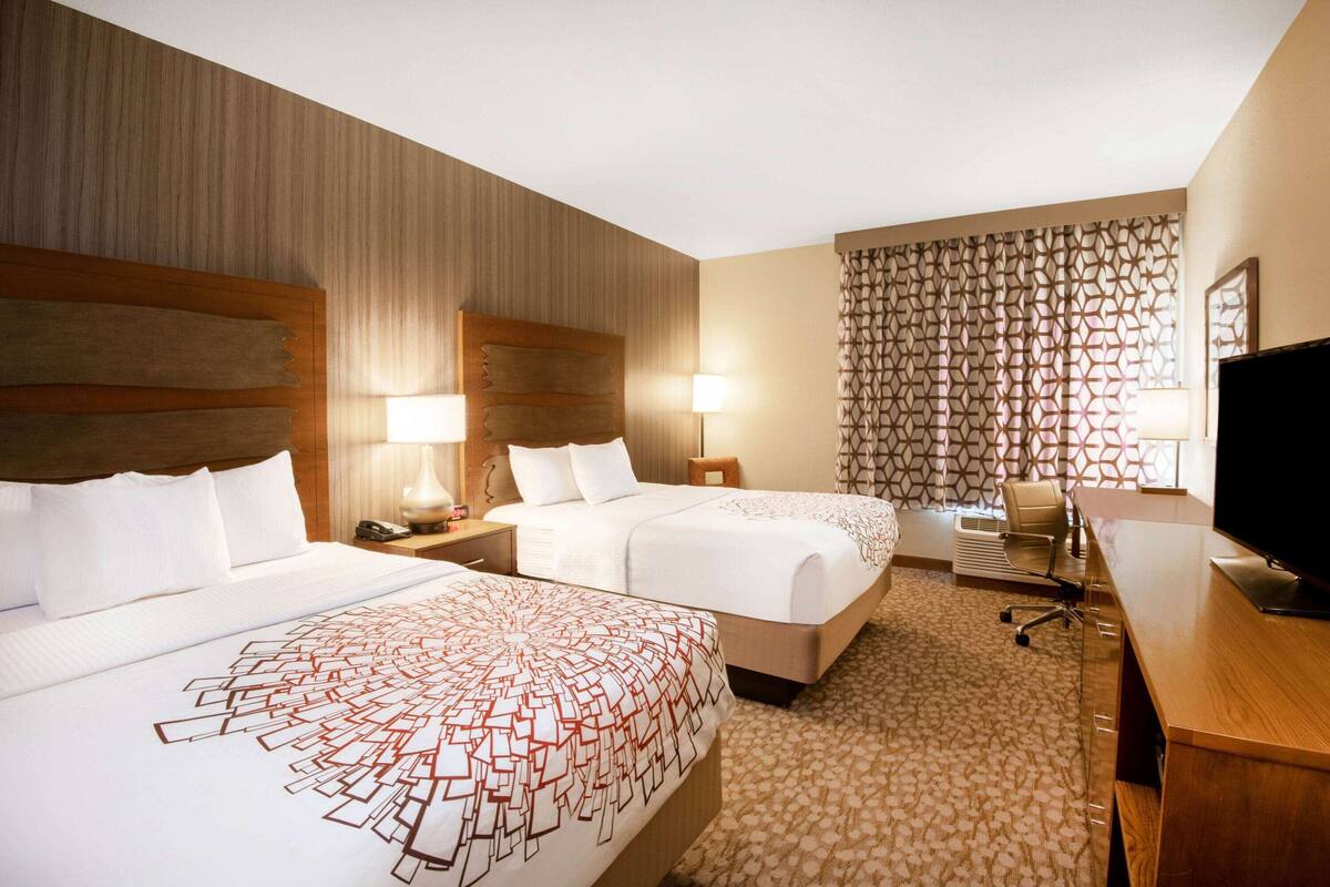 A hotel room with two beds, a desk, a TV, and a patterned curtain.
