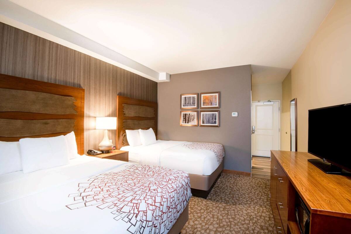 A hotel room with two beds, a TV, a desk, and a door leading to a bathroom.