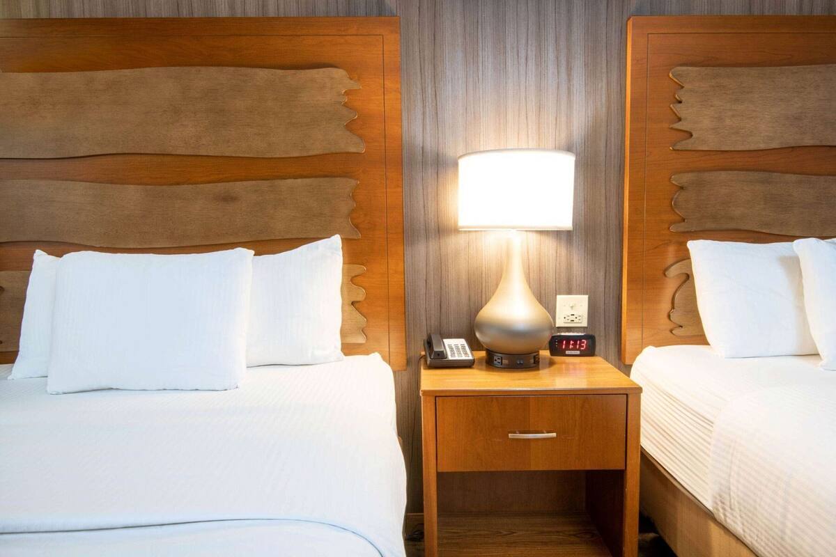 A hotel room with two beds, a nightstand with a lamp, a phone, and a digital clock.
