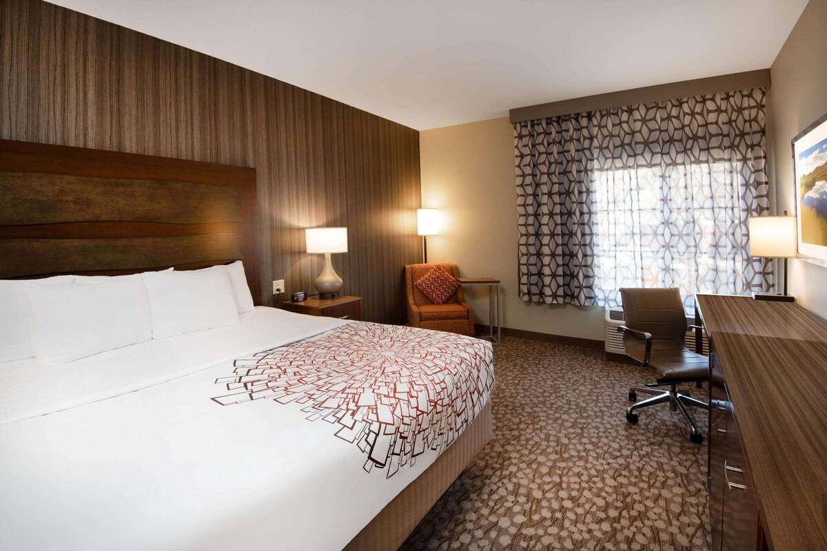 A hotel room with a large bed, a desk, a chair, a lamp, and a patterned curtain.