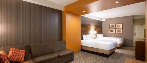 A hotel room with a sofa, a bed, a wooden nightstand, and a desk.