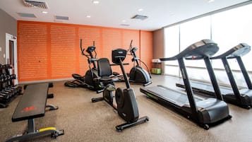 Et fitnessrum med forskellig træningsudstyr, herunder løbebånd, crosstrainer og bænk.