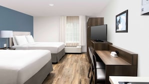 A hotel room with two beds, a desk with a chair, a television, and an air conditioning unit. - WoodSpring Suites Austin South Central I-35 (Austin)