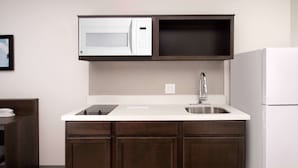 A compact kitchen with a microwave, sink, and a white refrigerator. - WoodSpring Suites Austin South Central I-35 (Austin)