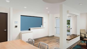 A modern conference room with a wooden table, chairs, a blue window, and a view of a parking area. - WoodSpring Suites Austin South Central I-35 (Austin)