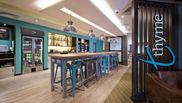 Een bar met een lange toonbank en meerdere krukken, een koeltoog en een bord met de naam 'thymine'.