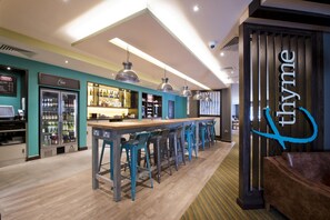 Una zona de bar con una barra alargada y varios taburetes, un mostrador refrigerado y un letrero con el nombre 'thymine'.