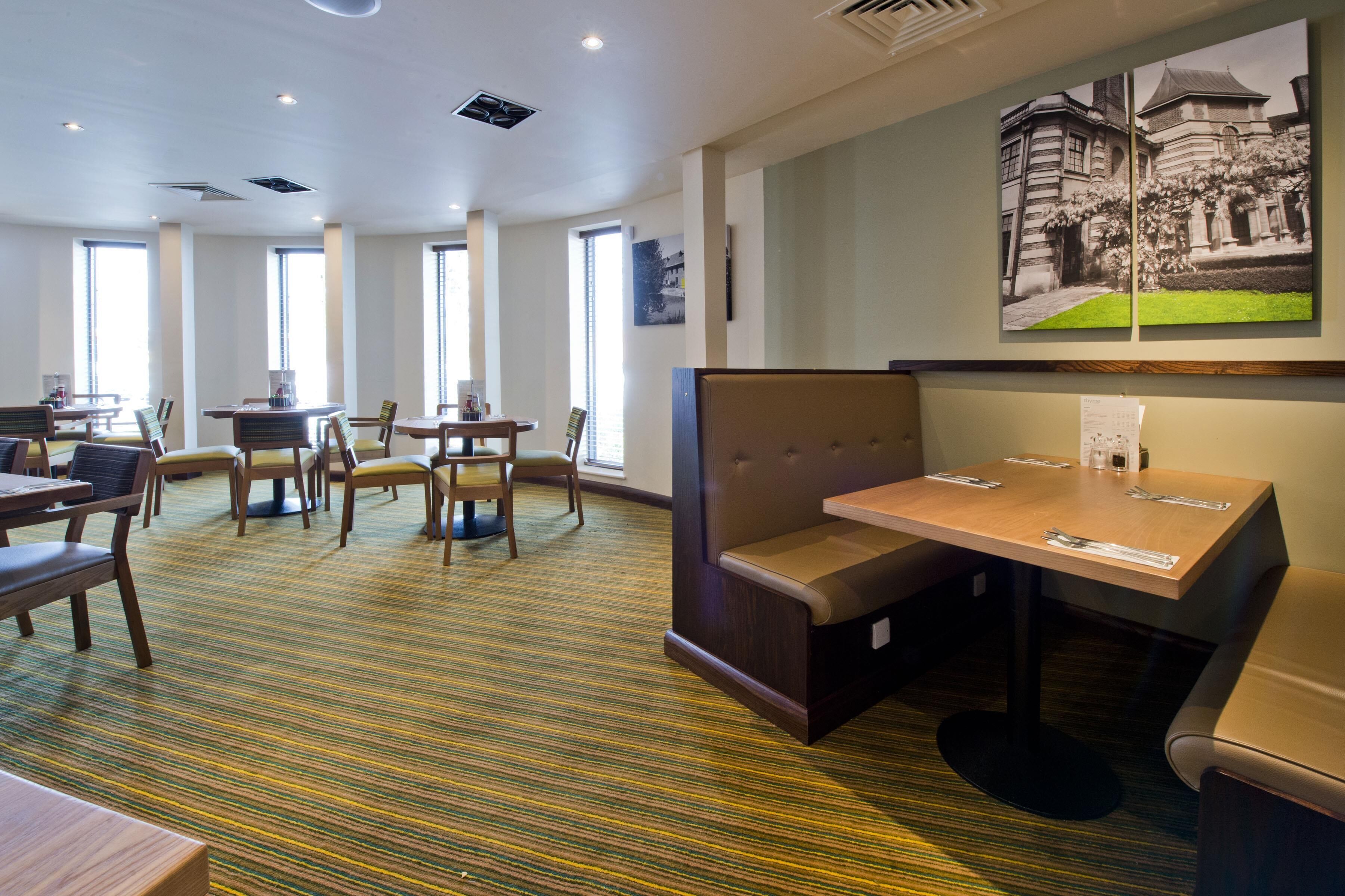 En hotellobby med flera sittgrupper, inklusive avskilda bås och bord, samt stora fönster som släpper in naturligt ljus.