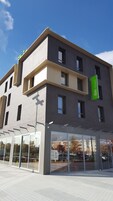 A modern building with a prominent green sign, large windows, and a clear sky.