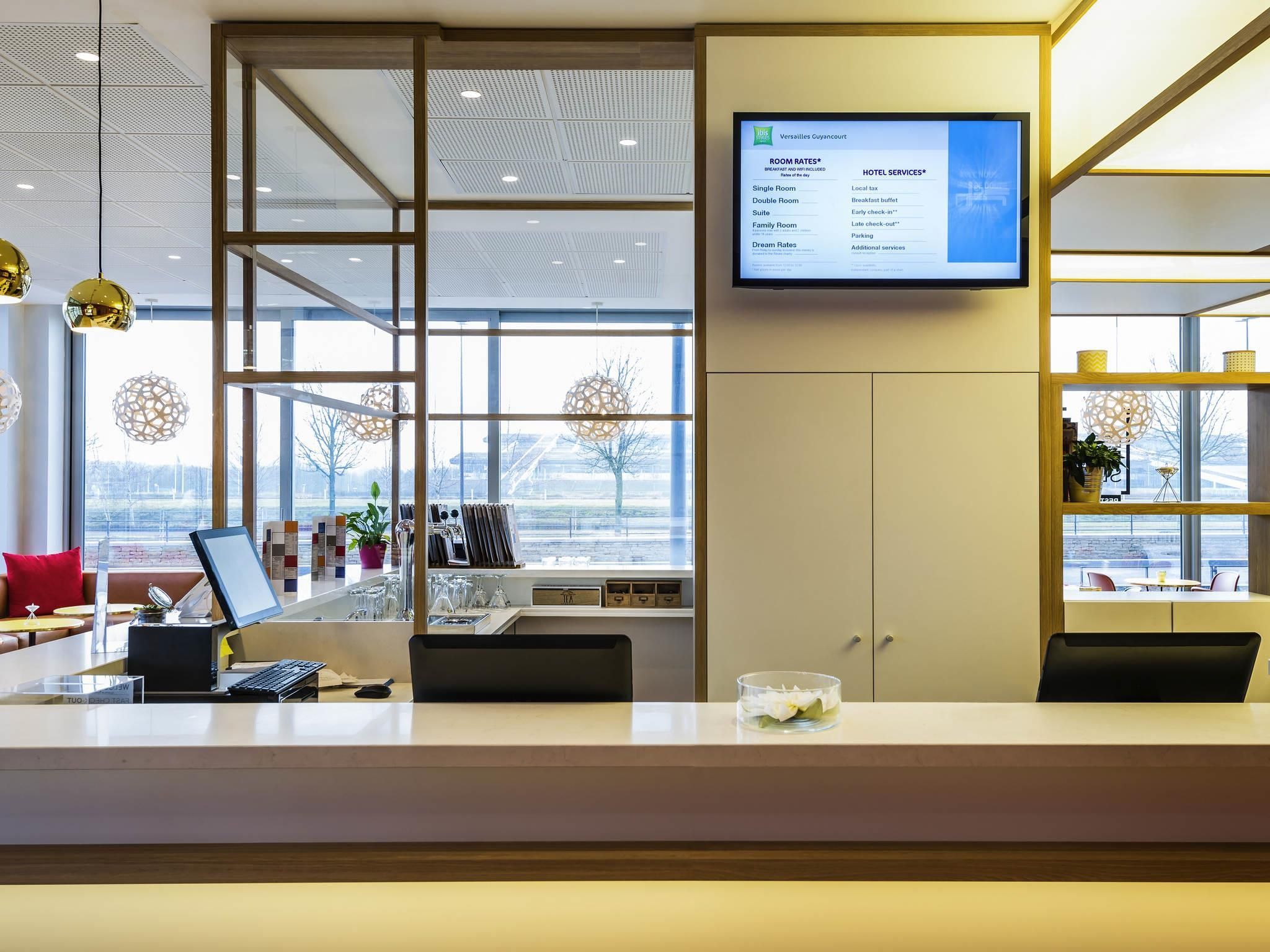 Zona de recepción de hotel con pantalla digital que muestra tarifas y servicios, amplias ventanas con vistas al exterior y un diseño interior moderno.