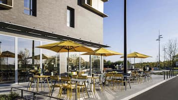 Un caffè all'aperto con sedie e ombrelloni gialli, un edificio in mattoni e cielo sereno.