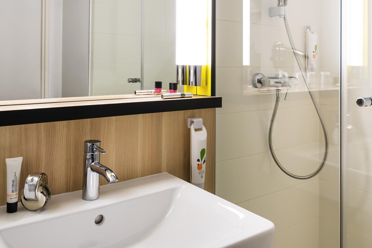 Een badkamer met een witte wastafel, een chromen kraan en een douchecabine van glas.