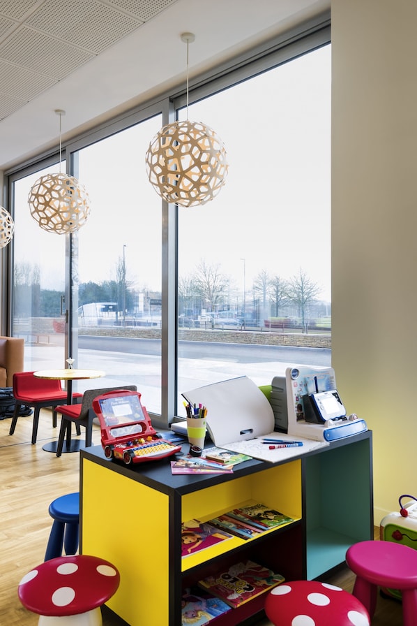 A modern children's play area with colorful furniture, a desk with educational materials, and large windows offering a view of the outside. - ibis Styles Versailles Guyancourt (Guyancourt)